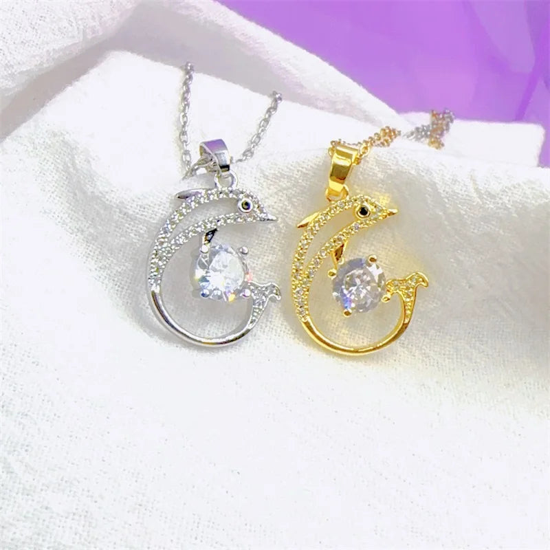 Two necklaces with penguin pendants on crescent moon designs, one gold and one silver, on a white fabric background.