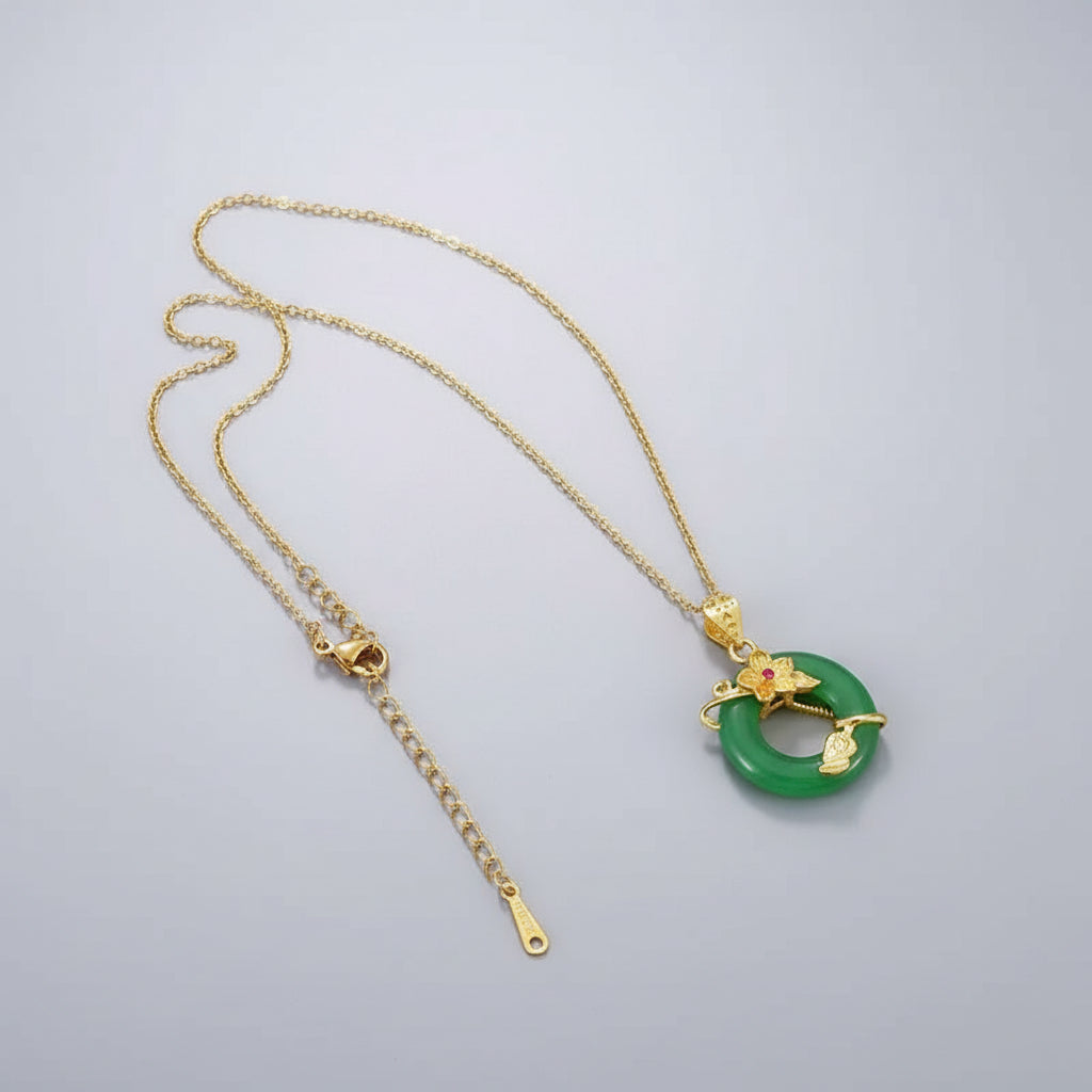 Gold necklace with a green pendant on a soft pink surface