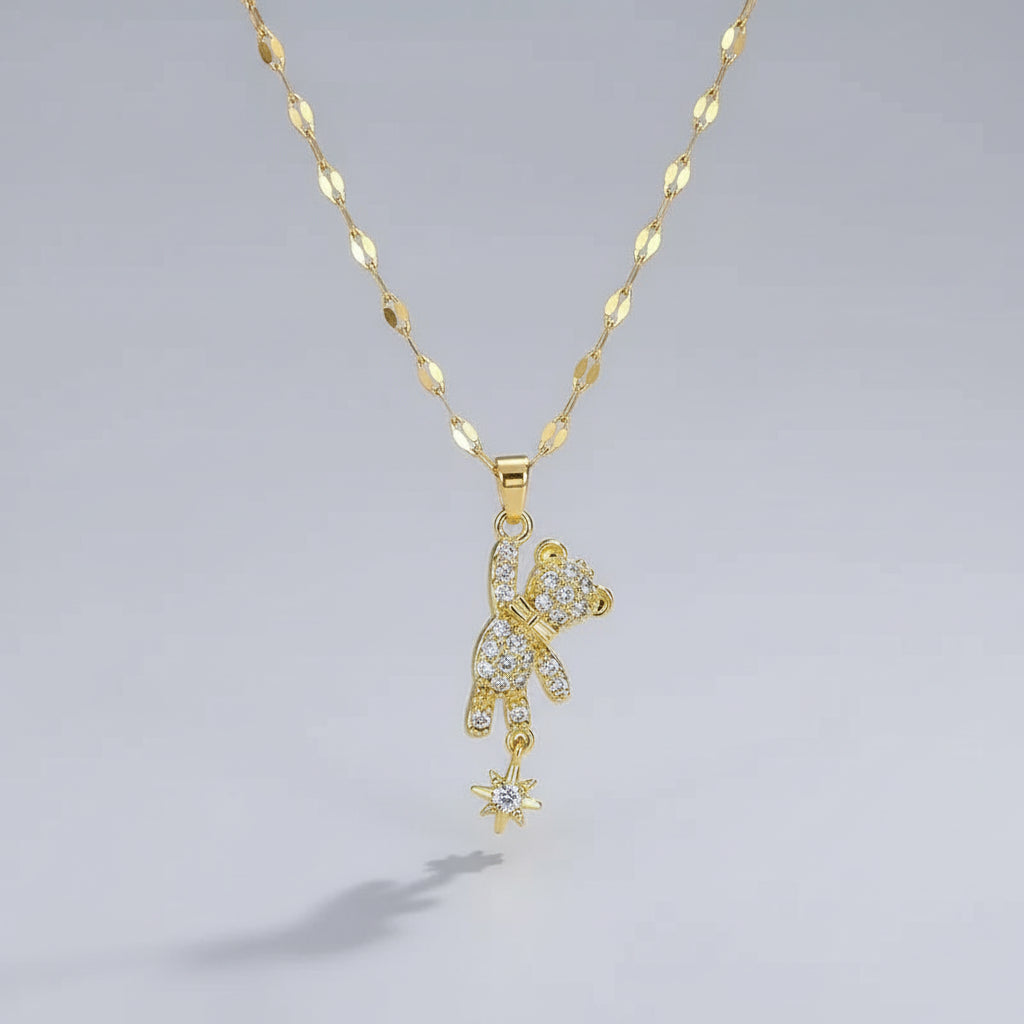 Gold teddy bear pendant necklace on a beige surface with white fabric background