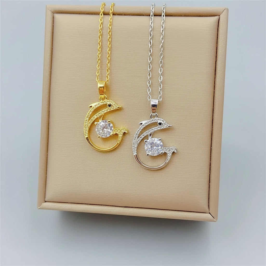 Two dolphin necklaces, one gold and one silver, on a beige display box.