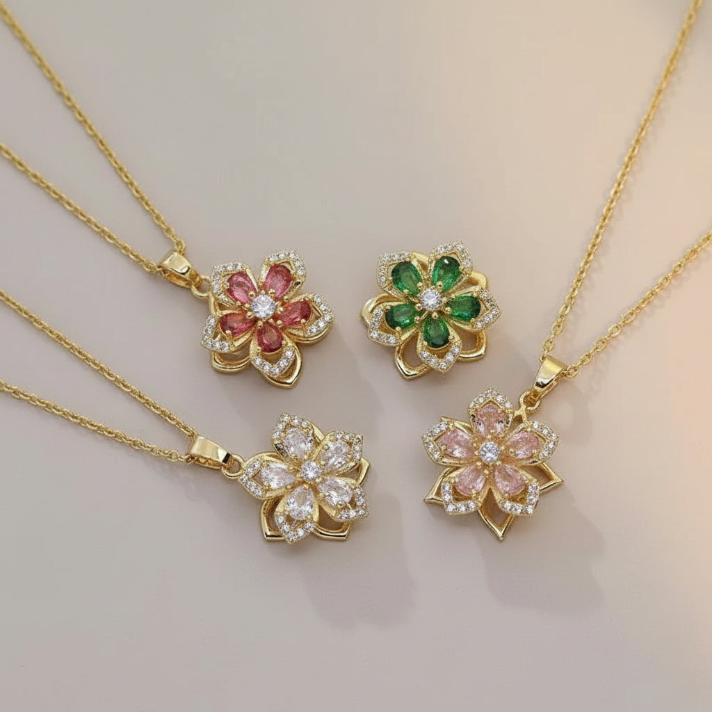 Gold necklaces with floral pendants featuring colorful gemstones on a beige surface.